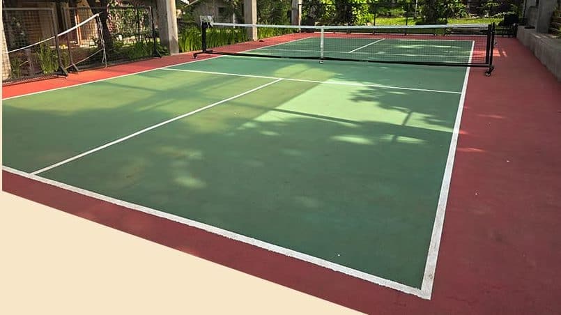 The court in daylight, shaded by trees and enclosed by greenery